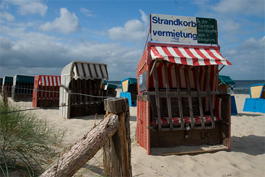 Strandkörbe am Strand, die mit einem Holzlattenrost verschlossen sind.