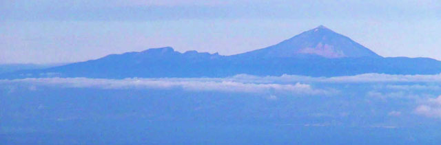 Ein spitzer Vulkankegel ragt in der Ferne aus dem Wolken heraus
