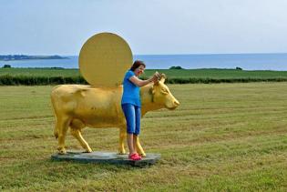 Das Modell einer goldfarbenen lebensgroßen Kuh auf einem Feld; Claudia hält diese bei den Hörnern