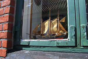 Altes FEnster mit grünem Holzrahmen, hinter dem ein Segelschiffsmodell steht