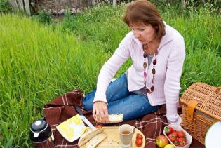 Claudia sitzt im Gras auf einer Decke, die mit Picknick-Leckereien gedeckt ist.