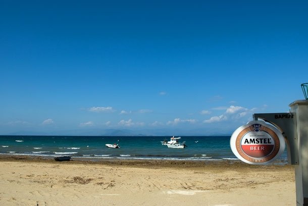 Sandstrand mit Booten, die davor ankern. Rechts ist ein Reklameschild von Amstel Beer