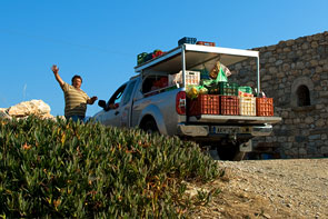 Ein Gemüsehändler steht neben seinem Gemüse-PKW und hebt grüßend seinen Arm