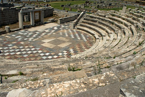 Halbkreisförmige Bühne umrahmt von aufsteigenden Sitzreihen. Der Bühnenboden besteht aus mosaikartig farblich unterschiedlichen Steinplatten.